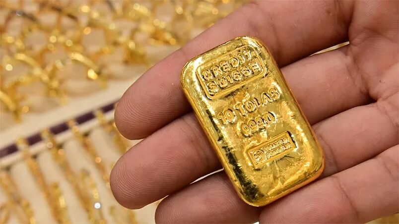 Thanh vàng được cầm trên tay với nền là nhiều vòng vàng khác.