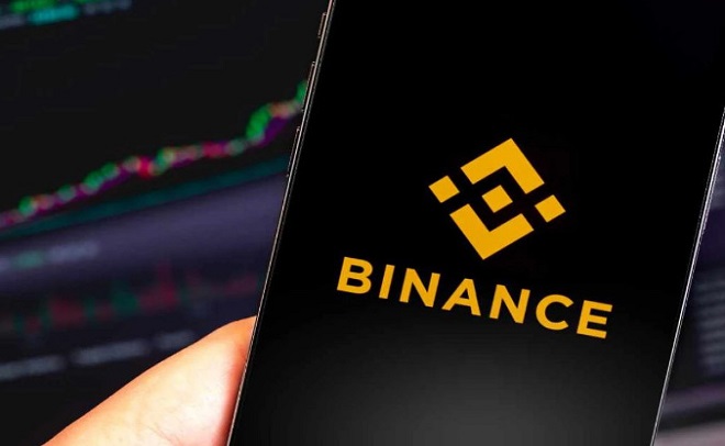 Điện thoại hiển thị logo Binance, nền là biểu đồ tài chính.