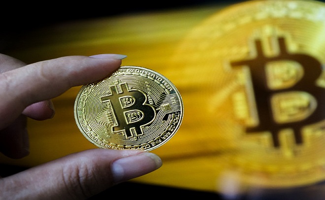 Một người đang cầm một đồng xu Bitcoin màu vàng trước nền mờ.