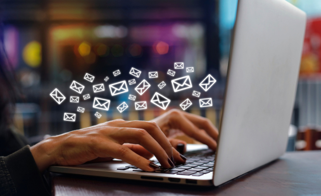 Người đang gõ trên máy tính xách tay với các biểu tượng email bay ra từ màn hình.