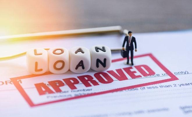 Giấy tờ cho vay với chữ "APPROVED" và mô hình người đàn ông nhỏ đứng cạnh khối chữ "LOAN".