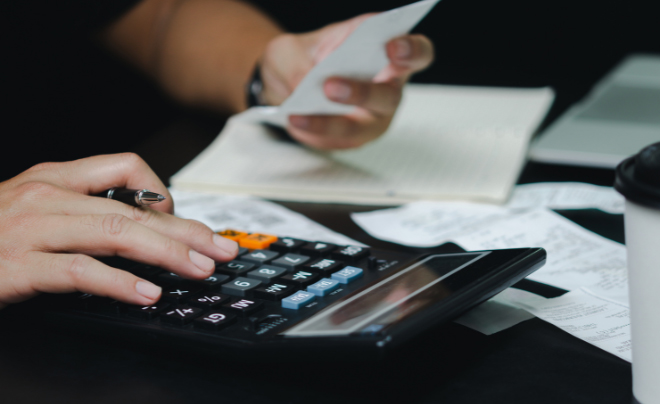 Người sử dụng máy tính cầm hóa đơn, ghi chú bên cạnh, tập trung vào tính toán tài chính trên bàn.
