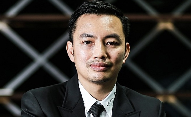 Người đàn ông mặc vest đen, áo sơ mi trắng, nhìn phía trước với phông nền tối.
