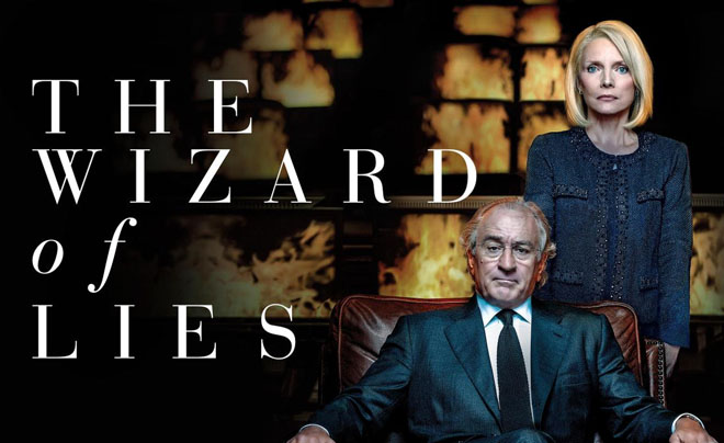 Hai người ngồi và đứng trước nền tối có chữ "The Wizard of Lies", người đàn ông mặc vest, người phụ nữ mặc áo khoác.