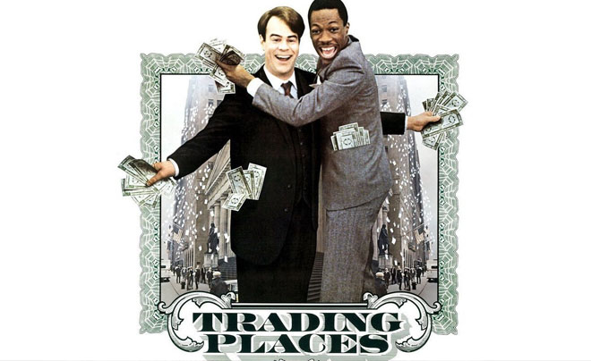 Hai người đàn ông mặc vest cầm tiền, đứng trước bối cảnh thành phố và dòng chữ "Trading Places".