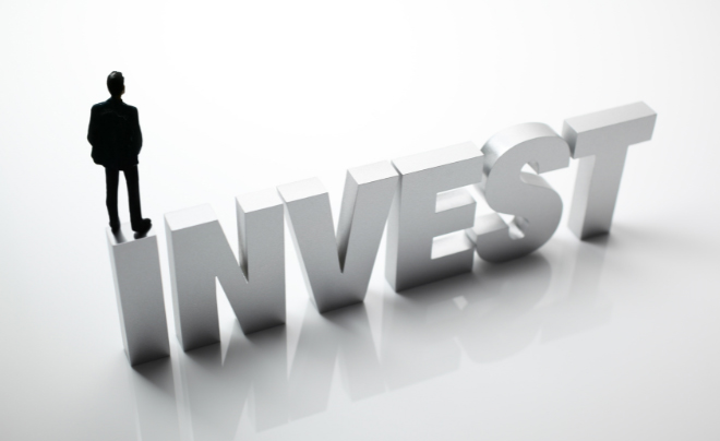 Một người đứng cạnh chữ "INVEST" lớn trên nền trắng, biểu thị khái niệm đầu tư.