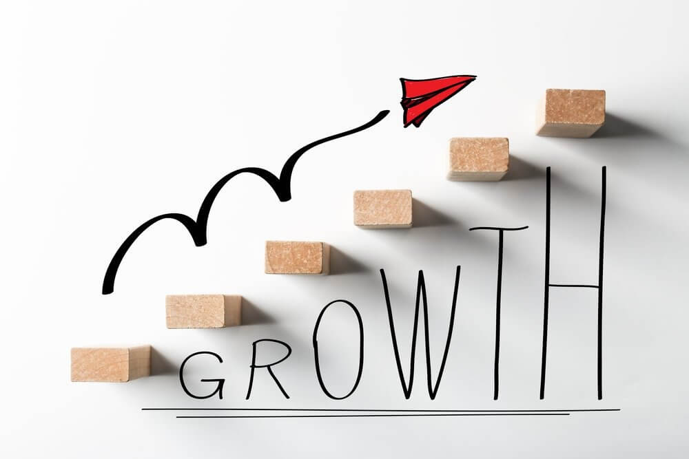 Khối gỗ xếp thành bậc thang, chữ "GROWTH" và hình vẽ máy bay giấy biểu thị sự phát triển.