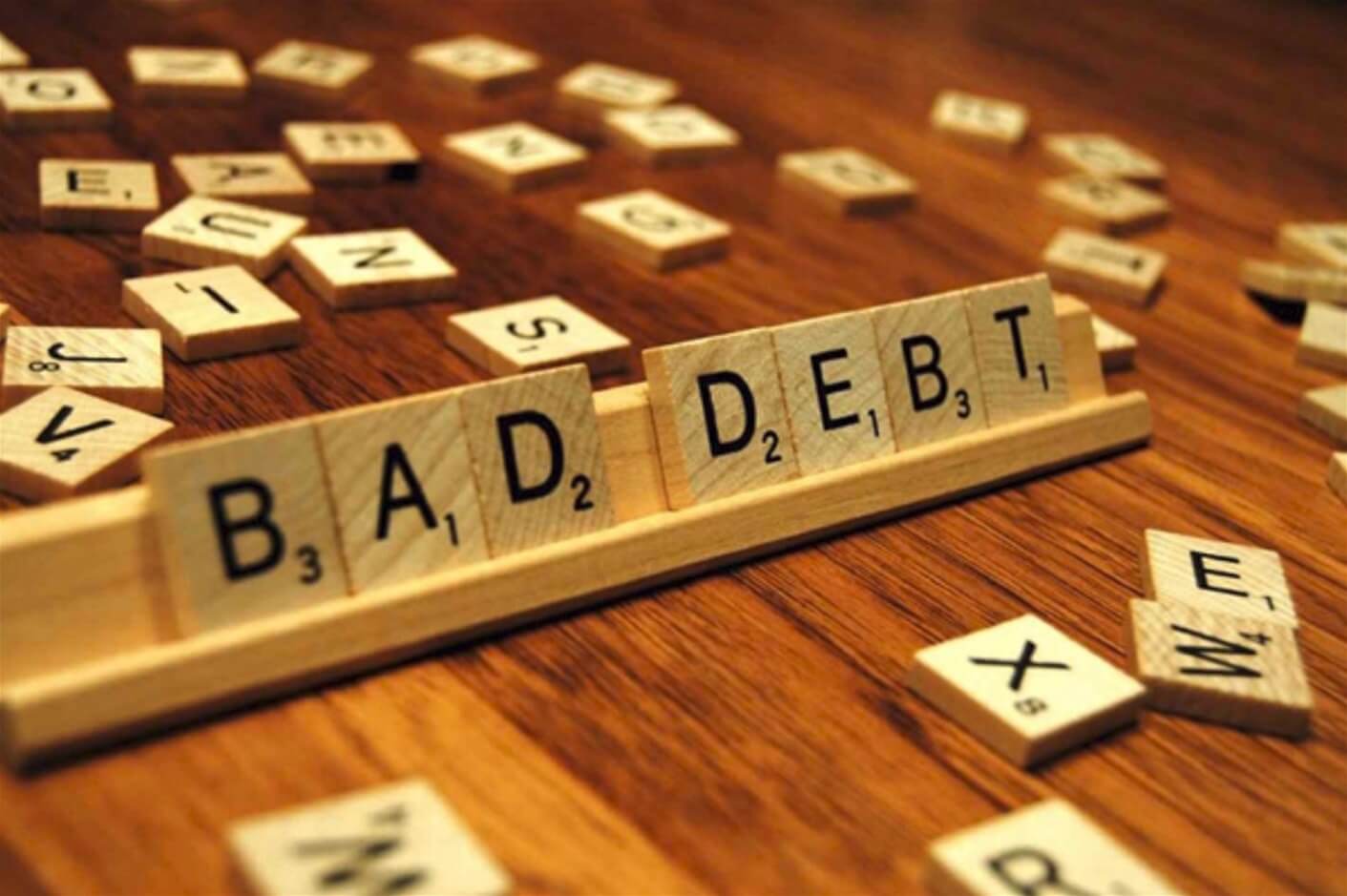 Các chữ cái trên miếng ghép trò chơi ghép thành từ "BAD DEBT" trên bàn gỗ.