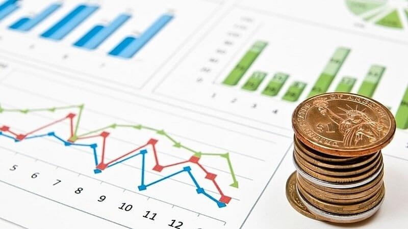 Biểu đồ tài chính với các thanh màu xanh, đỏ và chồng tiền xu bên cạnh trên nền trắng.