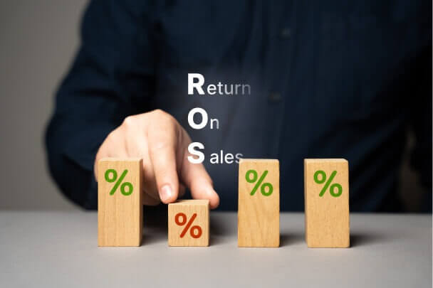 Người chỉ vào khối gỗ có ký hiệu phần trăm, với chữ viết tắt "ROS" và nội dung "Return On Sales".
