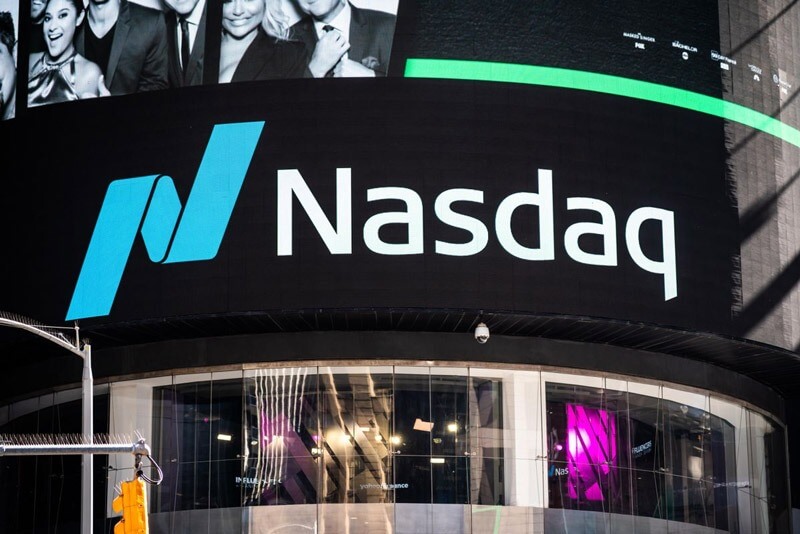 Màn hình lớn hiển thị logo Nasdaq tại một tòa nhà kính ở khu đô thị.