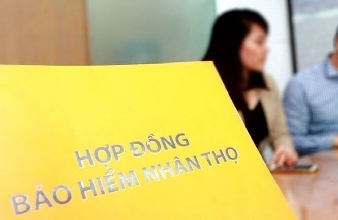 Chiến Lược Đầu Tư Hiệu Quả và An Toàn Với Thu Nhập 10 Triệu 7 Tài liệu hợp đồng bảo hiểm nhân thọ màu vàng, hai người ngồi phía sau trong phòng họp.