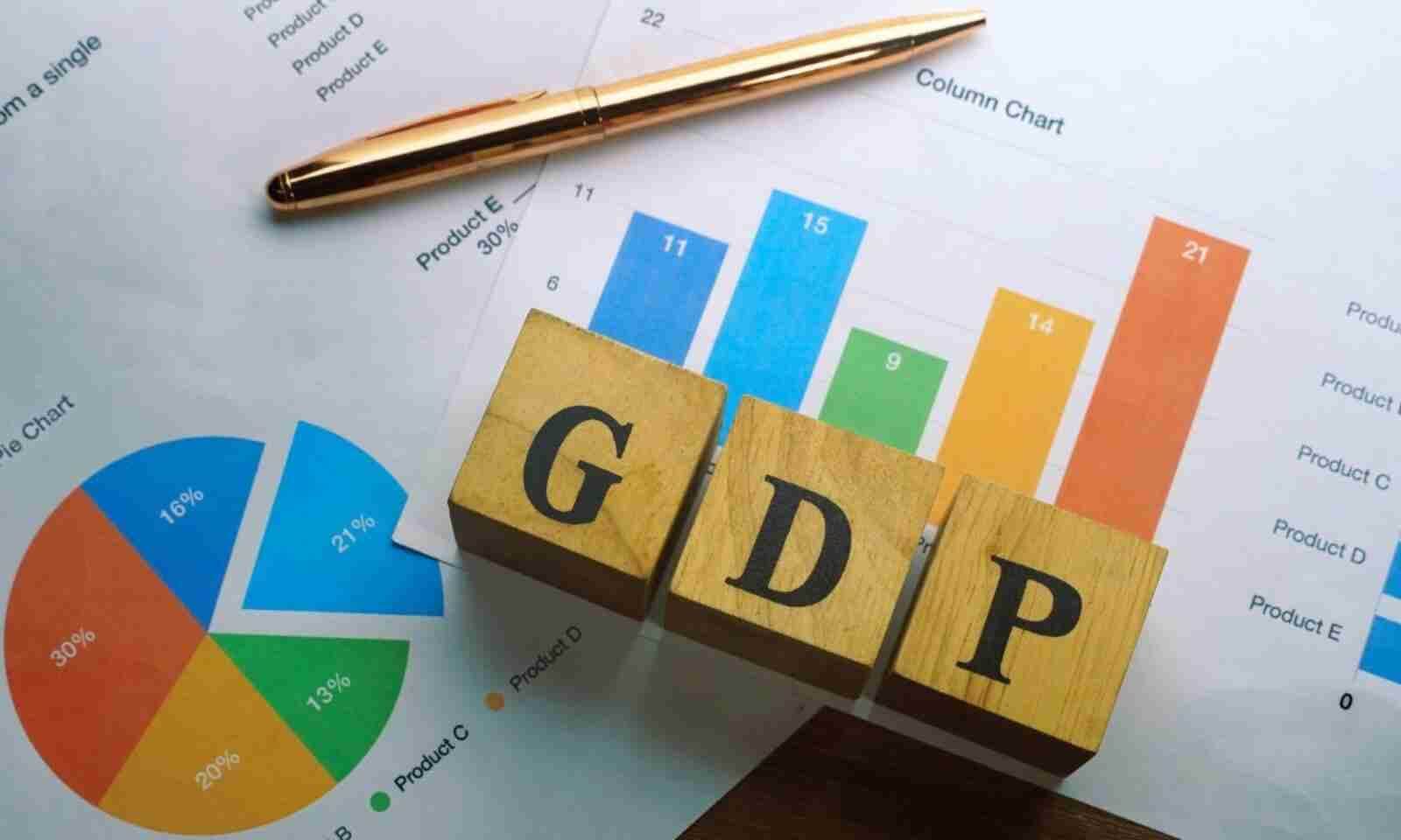 Khối gỗ chữ "GDP" trên biểu đồ cột và tròn, kèm bút màu vàng trên nền giấy trắng.