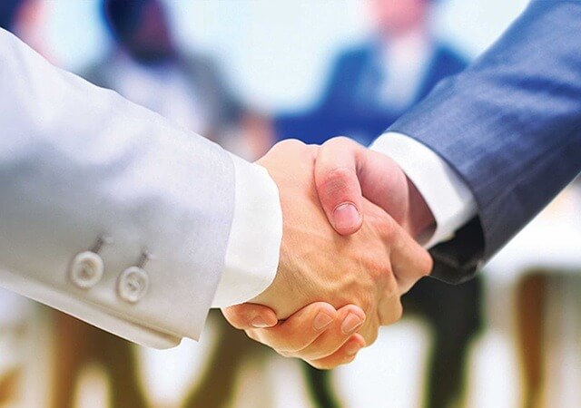Hai người bắt tay nhau trong khung cảnh văn phòng, thể hiện sự hợp tác và đồng thuận.