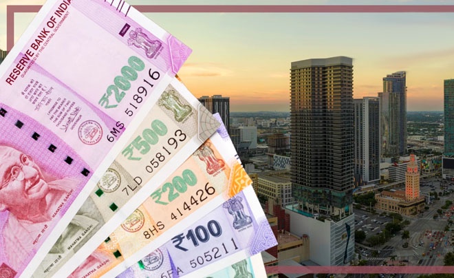 Tiền giấy Ấn Độ nhiều mệnh giá được đặt trước cảnh thành phố với các tòa nhà cao tầng lúc hoàng hôn.