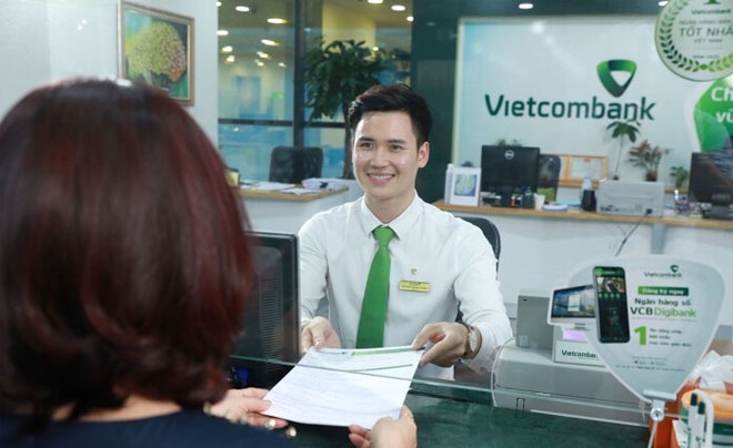 Nhân viên ngân hàng trao đổi tài liệu với khách hàng tại quầy giao dịch Vietcombank.
