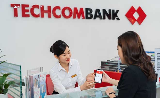 Nhân viên ngân hàng đang hướng dẫn khách hàng sử dụng ứng dụng trên điện thoại thông minh tại quầy giao dịch.