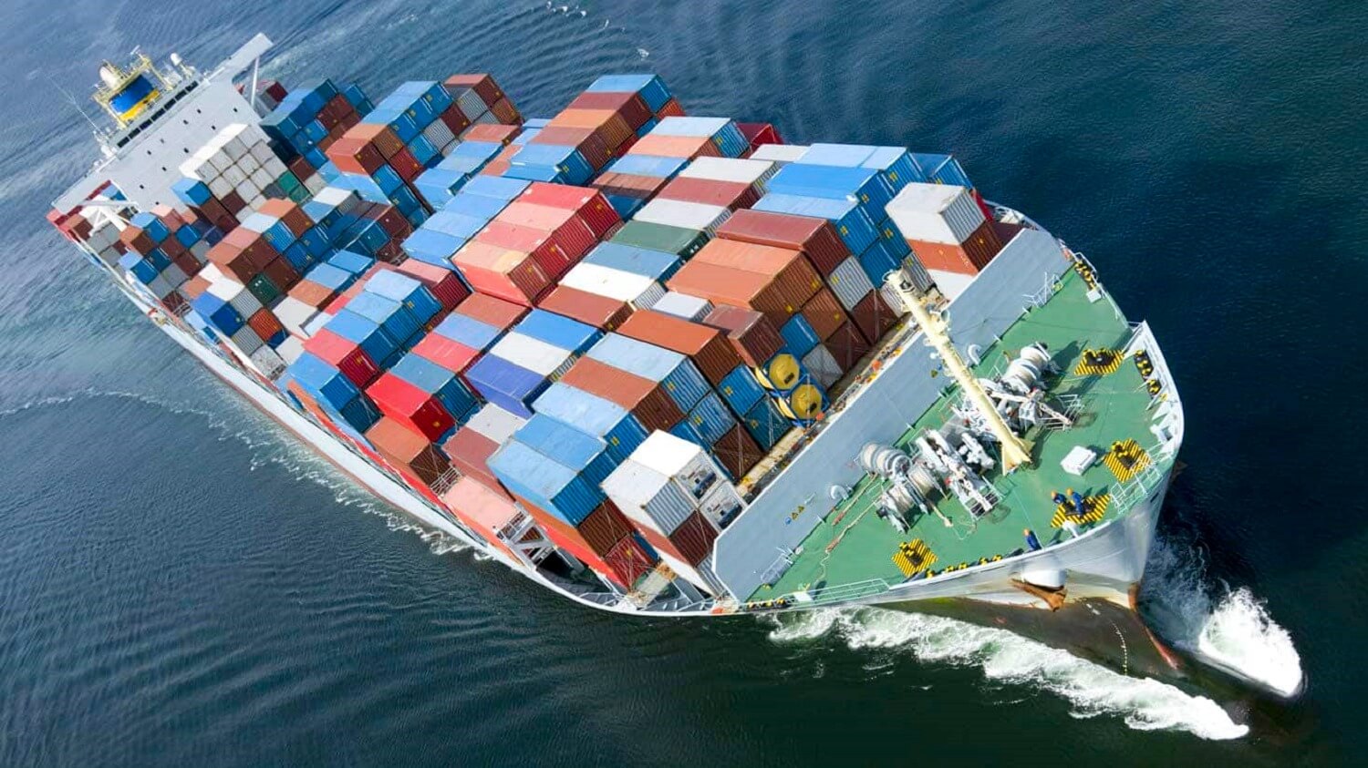 Tàu chở hàng lớn đang di chuyển trên biển, trên boong chứa nhiều container màu sắc khác nhau.
