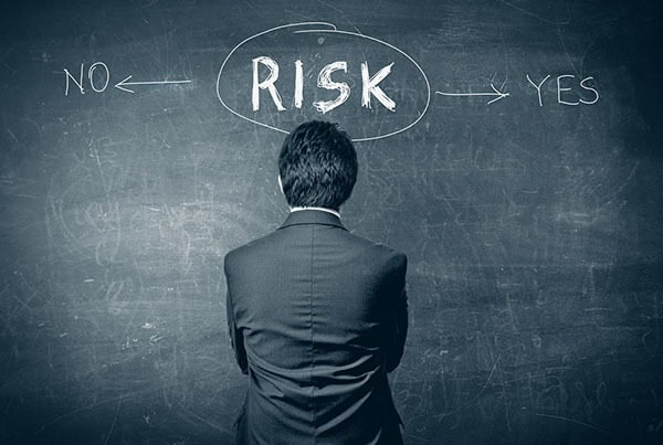 Người đàn ông đứng trước bảng đen với từ "RISK" ở giữa, và mũi tên chỉ "NO" và "YES".