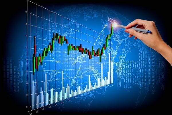 Biểu đồ tài chính với các cột và đường tăng, tay cầm bút chỉ vào điểm cao nhất trên nền bản đồ thế giới.