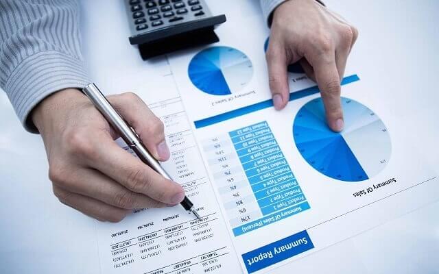Người đang phân tích biểu đồ và tài liệu tài chính trên bàn với máy tính cầm tay và bút.