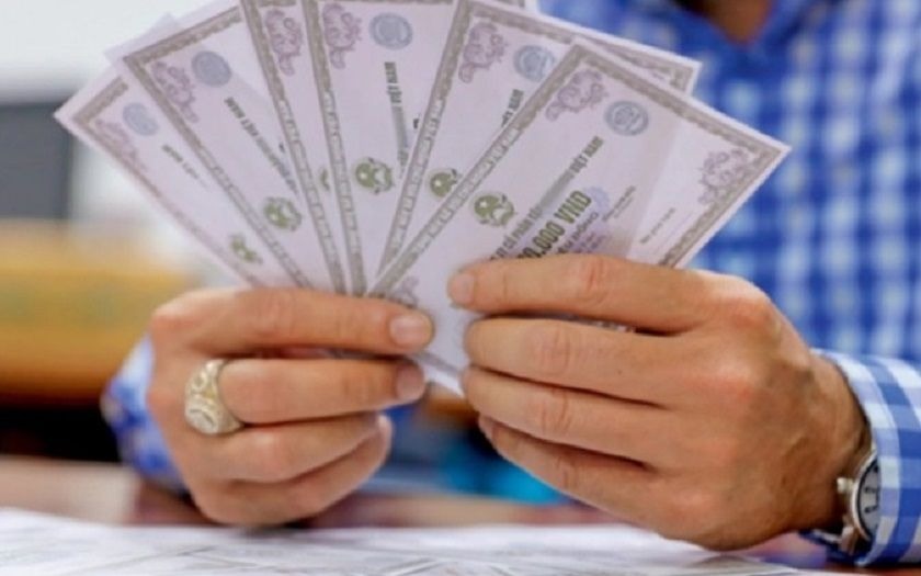 Người cầm nhiều tờ giấy chứng nhận tài chính, mặc áo sơ mi kẻ sọc xanh trắng.