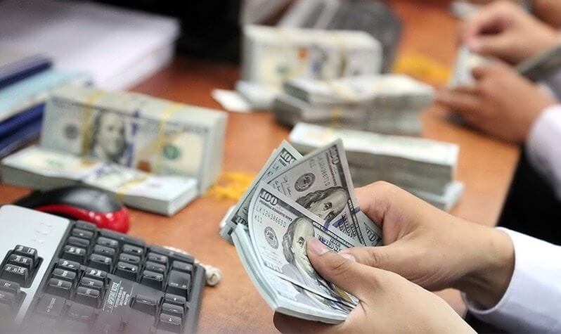 Người đang đếm các tờ đô la Mỹ trên bàn làm việc, bên cạnh là bàn phím máy tính và các cọc tiền khác.