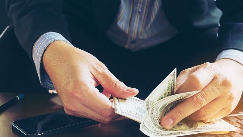 Người đang cầm và đếm tiền giấy, bên cạnh có điện thoại di động trên bàn.