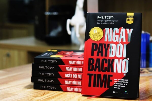 Sách "Ngày Đòi Nợ" của Phil Town, bản dịch tiếng Việt, xếp chồng trên bàn gỗ trong không gian nội thất.