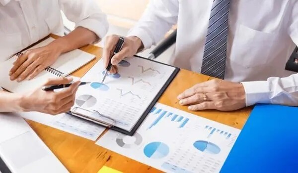 Hai người đang thảo luận về biểu đồ và tài liệu tài chính trên bàn làm việc gỗ.