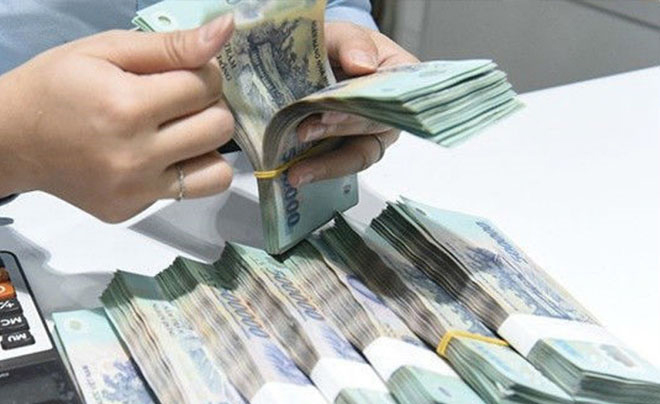 Người đang đếm một xấp tiền giấy Việt Nam trên bàn, bên cạnh máy tính cầm tay.