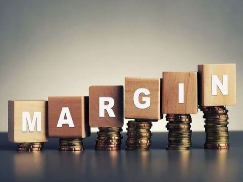 Các khối gỗ xếp thành chữ "MARGIN" trên các chồng tiền xu, biểu thị khái niệm tài chính.