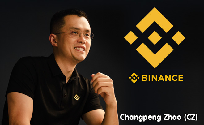 Người đàn ông ngồi cười, mặc áo đen có logo vàng, bên cạnh là logo và chữ "Binance".