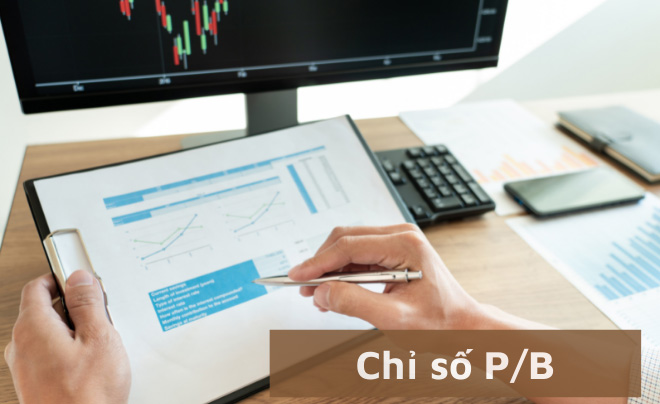 Người đang xem tài liệu phân tích tài chính với biểu đồ, màn hình máy tính hiển thị biểu đồ chứng khoán.