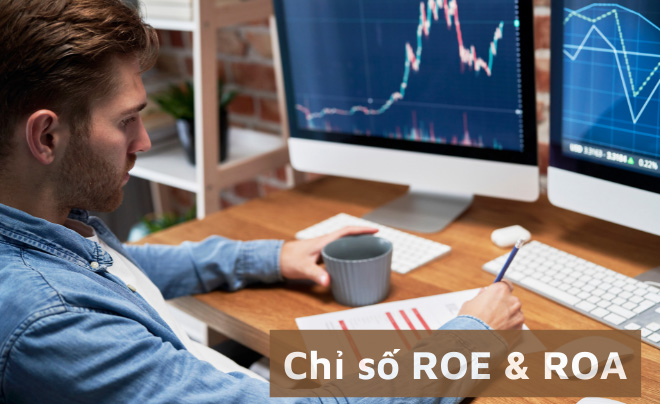 Người ngồi trước máy tính với biểu đồ tài chính trên màn hình, đang cầm cốc và xem tài liệu.