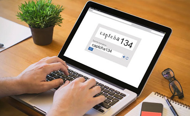 Người đang nhập mã CAPTCHA trên máy tính xách tay, bên cạnh là chậu cây và điện thoại.