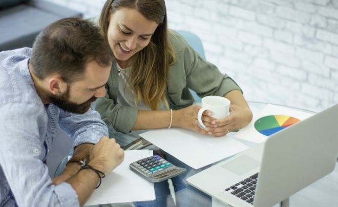 Hai người đang thảo luận tài chính trước máy tính xách tay, có máy tính cầm tay và biểu đồ tròn trên bàn.