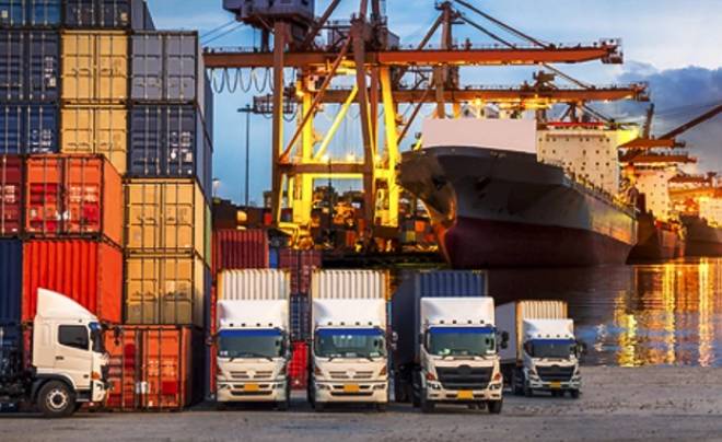 Cảng biển với cần cẩu, container và xe tải xếp hàng trước tàu hàng lớn dưới ánh sáng hoàng hôn.