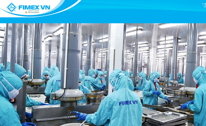 Công nhân trong trang phục bảo hộ màu xanh làm việc trong nhà máy chế biến thực phẩm với thiết bị hiện đại.