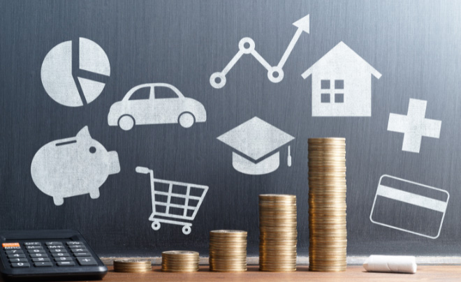 Các biểu tượng tài chính trên bảng đen với các cột tiền xu và máy tính phía trước, thể hiện kế hoạch tài chính.
