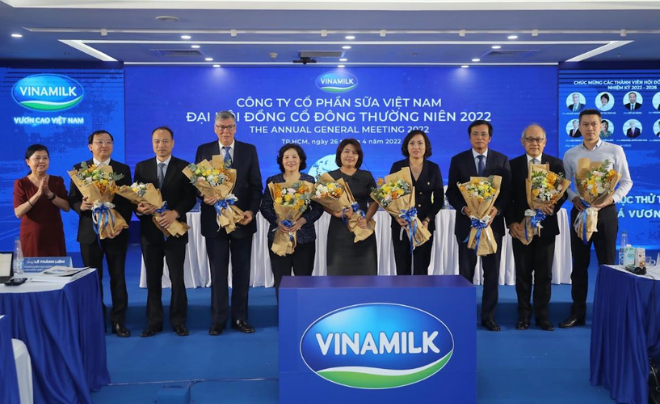 Nhóm người đứng trên sân khấu cầm hoa tại sự kiện công ty sữa, phía sau là màn hình lớn với logo Vinamilk.