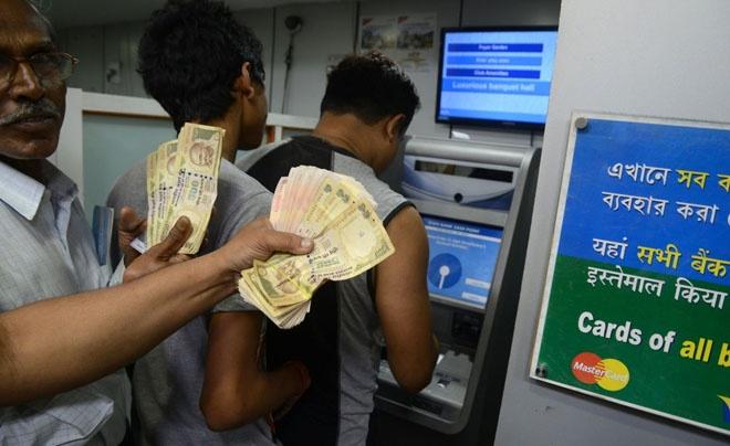 Người đang rút tiền từ máy ATM, với một người khác cầm nhiều tờ tiền giấy bên cạnh.