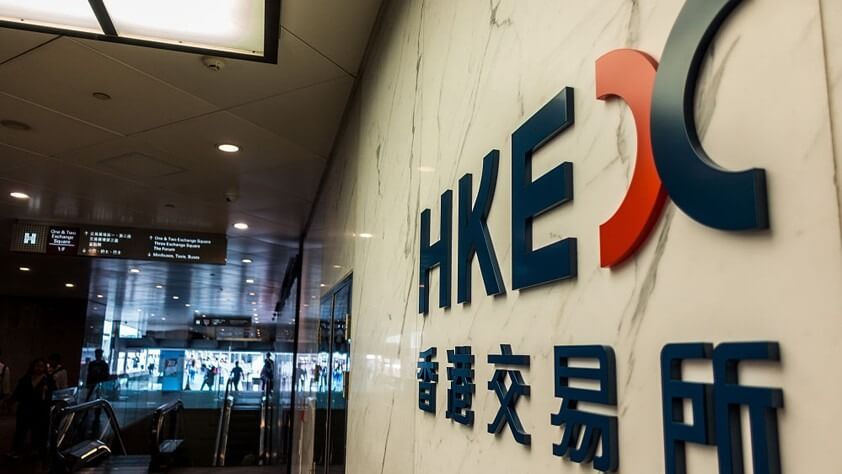 Biển hiệu HKEX trên tường trong một tòa nhà hiện đại, có người di chuyển ở phía xa.