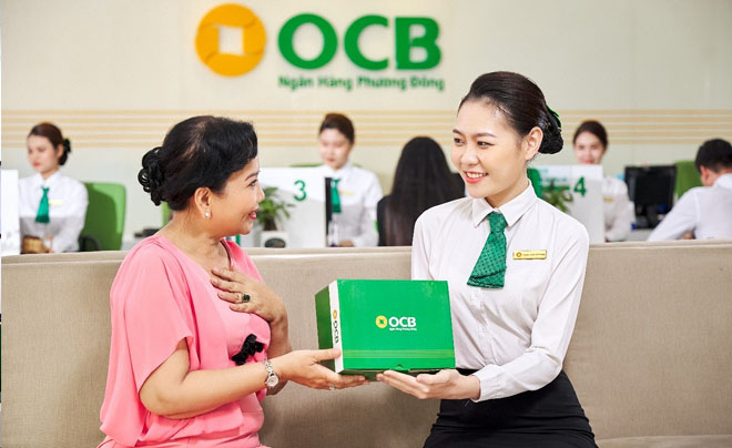 Nhân viên ngân hàng trao hộp quà cho khách hàng tại quầy giao dịch, với logo OCB phía sau.