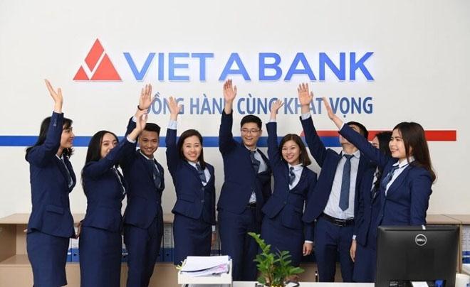 Nhóm người mặc đồng phục công sở đứng trước biển hiệu Viet A Bank, giơ tay lên cao, thể hiện tinh thần đồng đội.