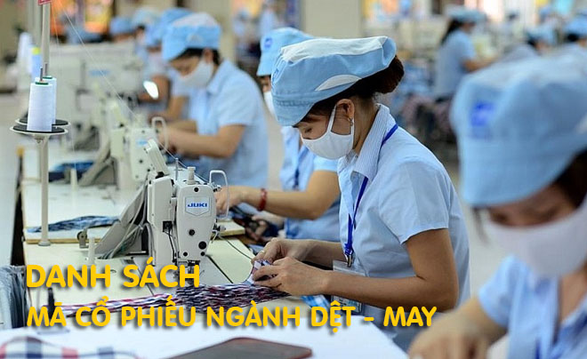 Công nhân trong nhà máy dệt may đang sử dụng máy may, tất cả đều mang khẩu trang và đồng phục màu xanh.