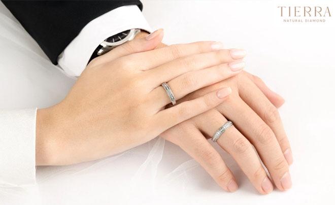 Hai bàn tay đeo nhẫn cưới trên nền trắng, một tay mặc áo vest và tay kia mặc áo trắng.