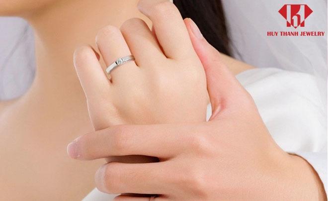 Hai tay đan vào nhau, một tay đeo nhẫn kim cương, nền trắng, có logo Huy Thanh Jewelry ở góc trên.