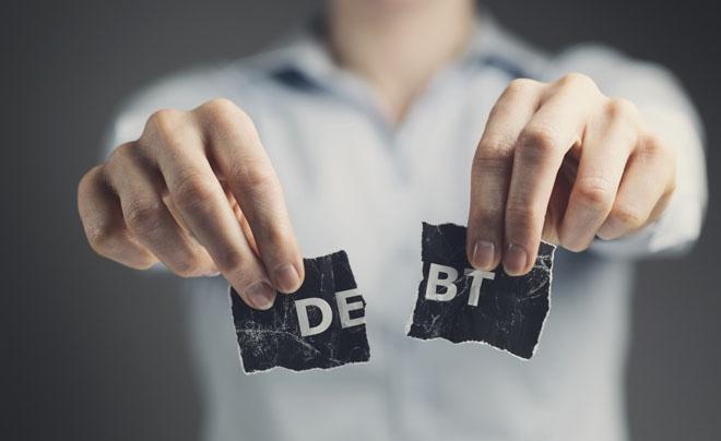 Người cầm hai mảnh giấy xé rời, mỗi mảnh có chữ "DE" và "BT", tạo thành từ "DEBT".