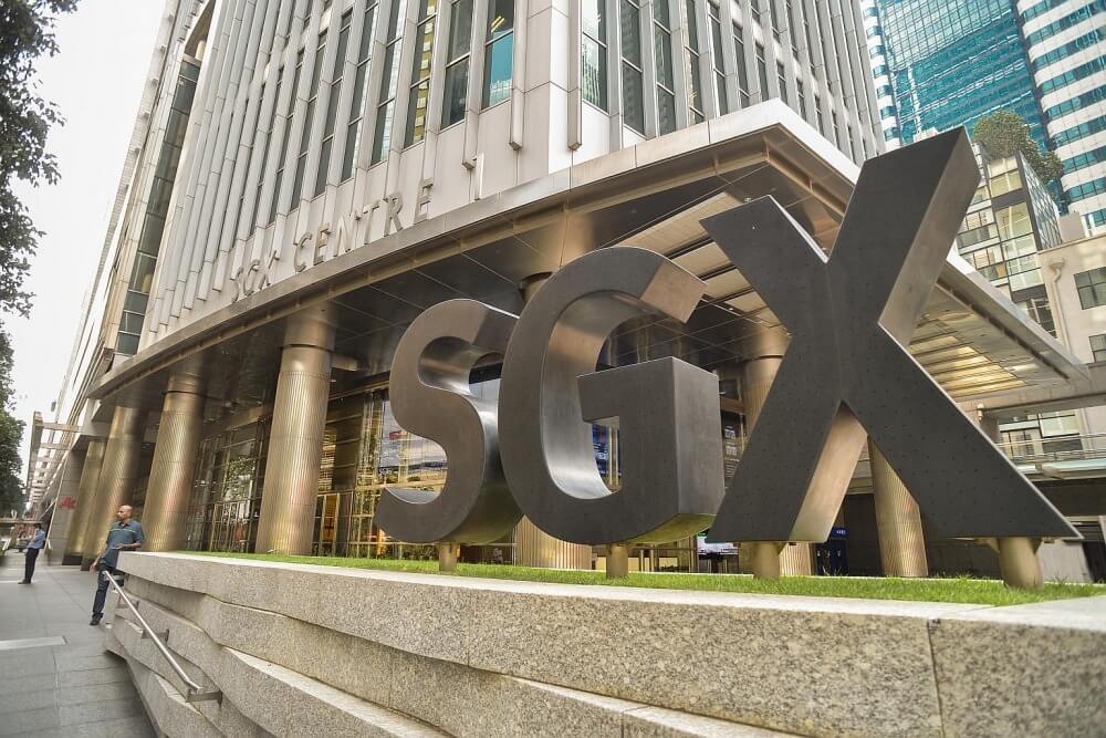 Tòa nhà với chữ SGX lớn phía trước, có người đi bộ và các cửa kính phản chiếu ánh sáng từ bên ngoài.